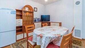 A compact room with a dining table, chairs, a television, a refrigerator, and a cabinet with glass doors. - Apartments Vukelic (Senj)