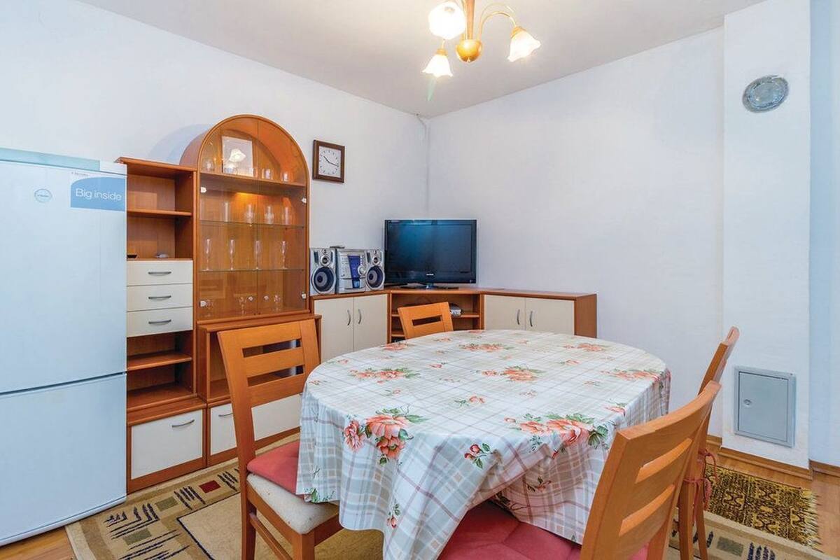 A compact room with a dining table, chairs, a television, a refrigerator, and a cabinet with glass doors.