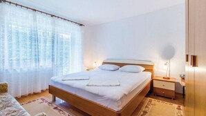 A neatly made bed with white linens, a wooden headboard, and a bedside table with a lamp. - Apartments Vukelic (Senj)
