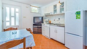 A compact kitchen with white cabinets, a refrigerator, a stove, and a television. - Apartments Vukelic (Senj)