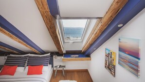 Une chambre dotée d’une lucarne, de poutres en bois, d’un lit avec une literie à rayures, d’une petite table et d’œuvres d’art accrochées aux murs.