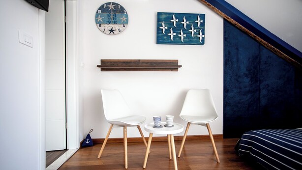 A modern room with two white chairs, a small table, a clock, and a blue artwork on the wall. - Apartments Porto Duce (Duce)