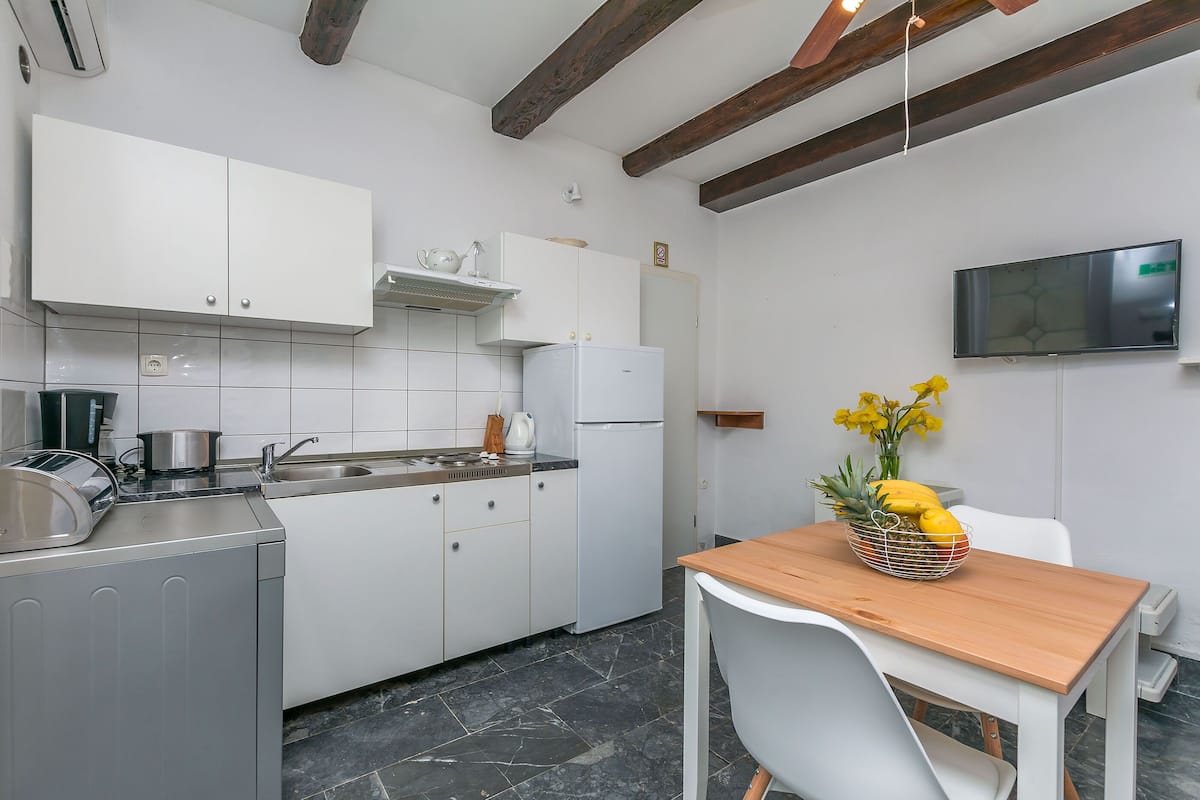 A modern kitchen with white cabinets, a stainless steel refrigerator, a wooden table, and a white chair.
