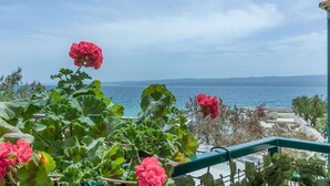 Un balcon orné de fleurs rouges et offrant une vue sur la mer.