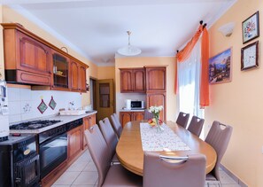 A kitchen with wooden cabinets, a stove, and a dining table with chairs. - Apartments Vesna (Rab)