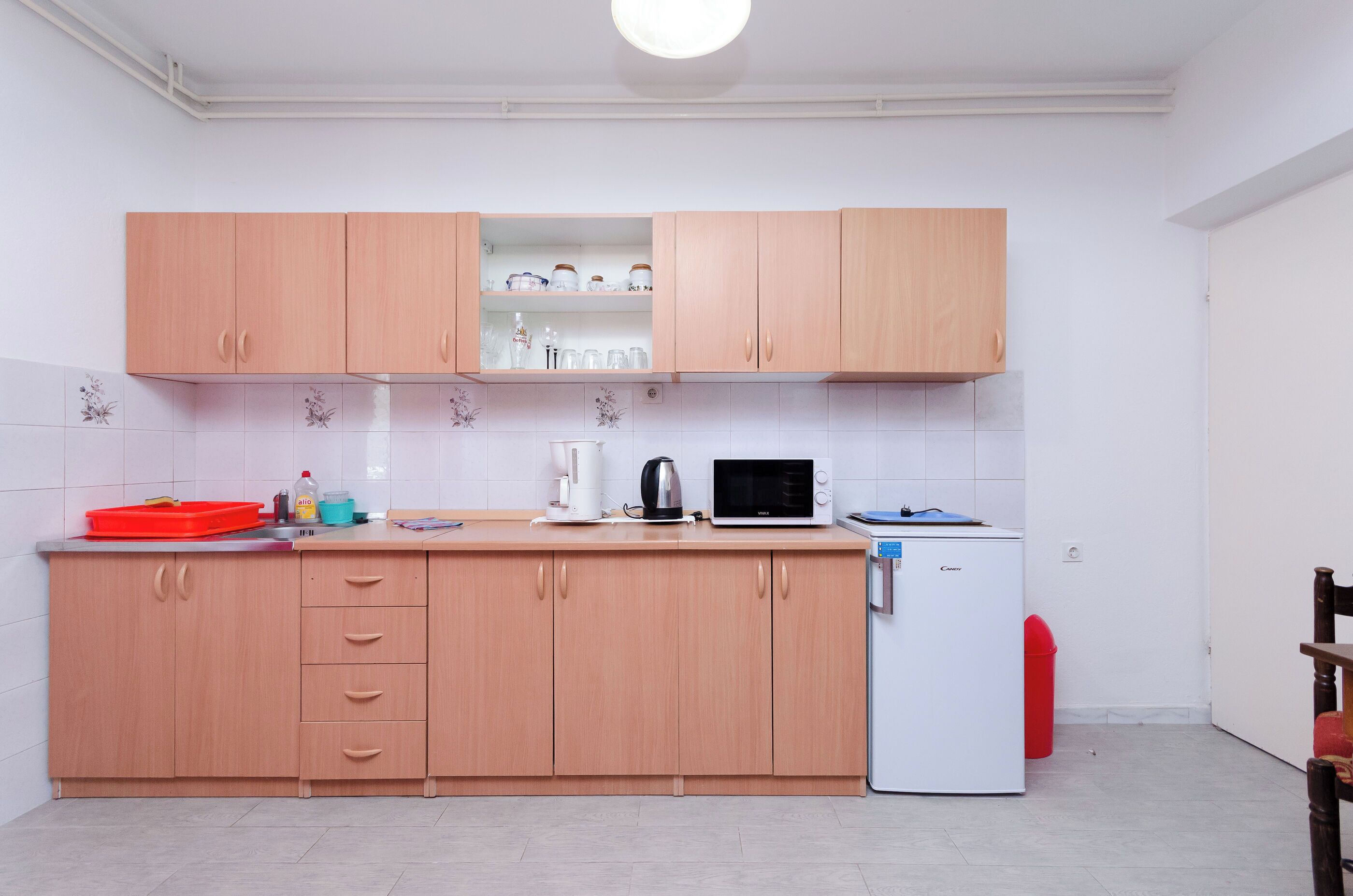 A compact kitchen with wooden cabinets, a microwave, a kettle, and a refrigerator.
