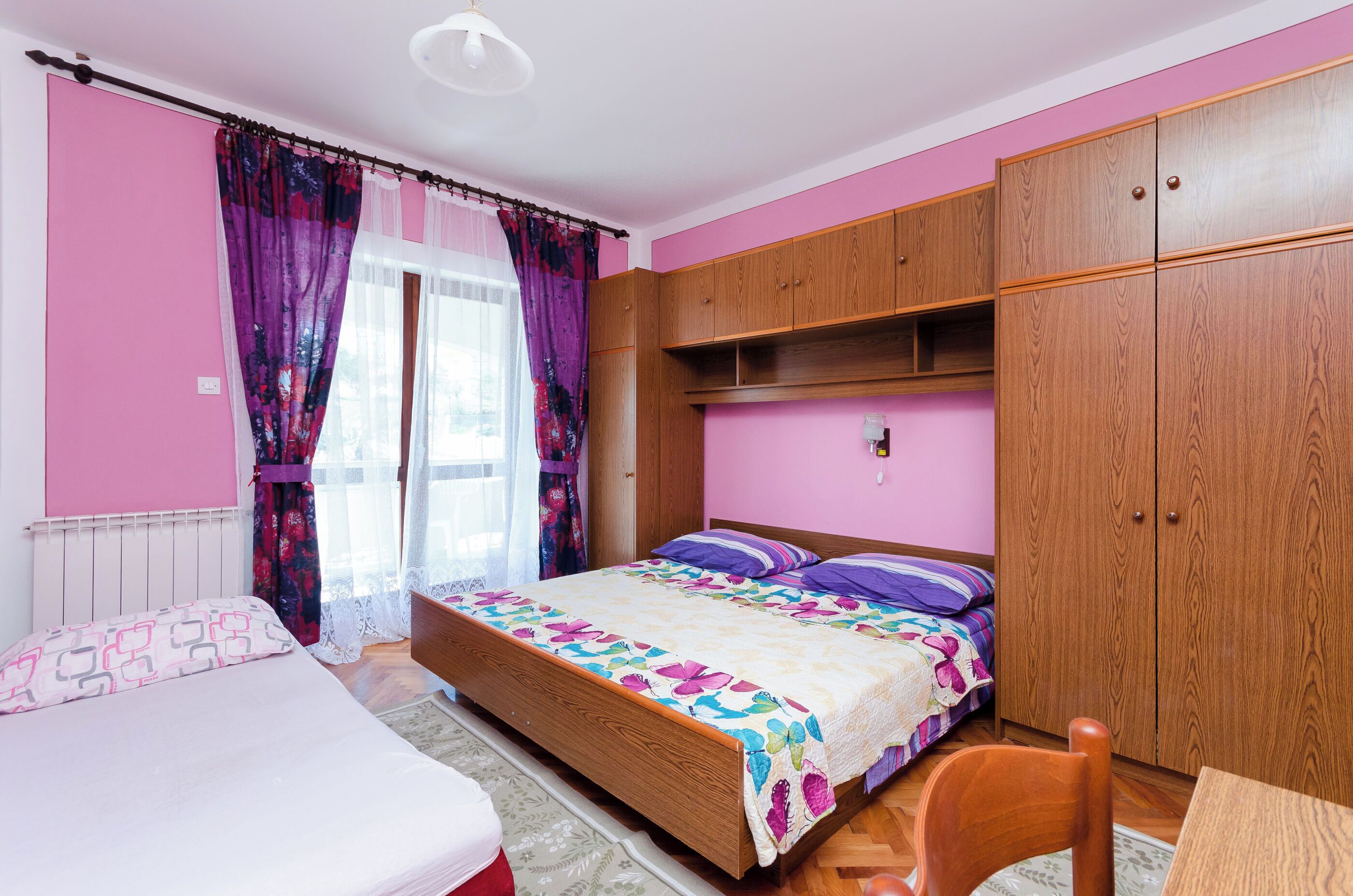A bedroom with a bed, a wooden wardrobe, and a desk.