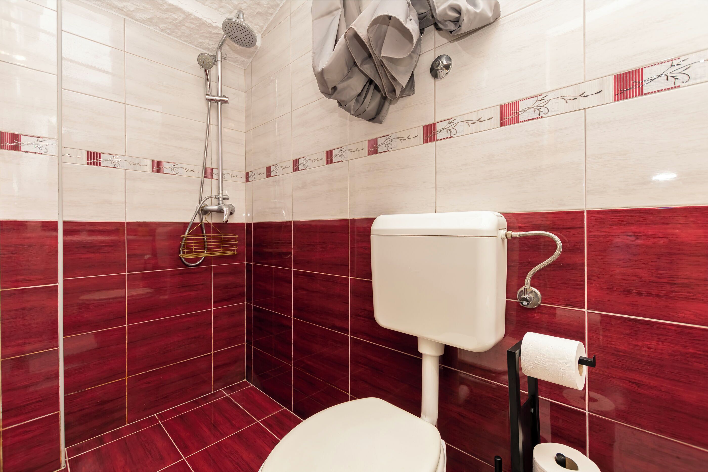 Un baño con azulejos rojo y blanco, una ducha, un inodoro y un perchero para toallas.