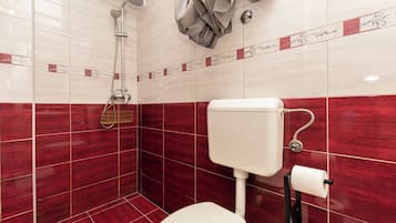 Un baño con azulejos rojo y blanco, una ducha, un inodoro y un perchero para toallas.