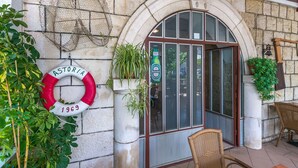 A stone building with a large arched entrance, a lifebuoy hanging on the wall, and potted plants near the entrance. - Apartments Cash and Dash (Krilo Jesenice)