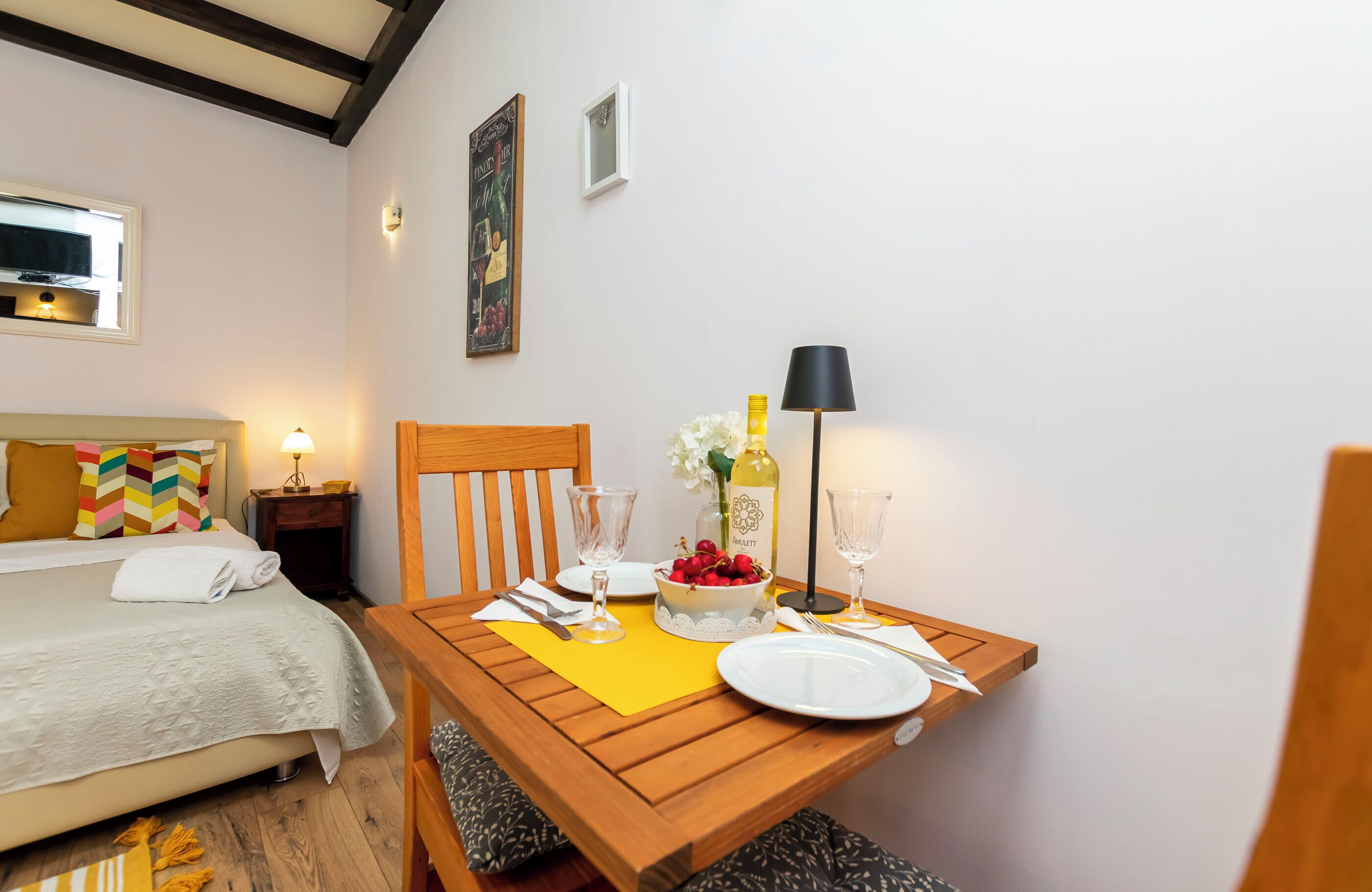 Un dormitorio ordenado con cama, mesita de noche y una zona de comedor con una mesa preparada para dos.