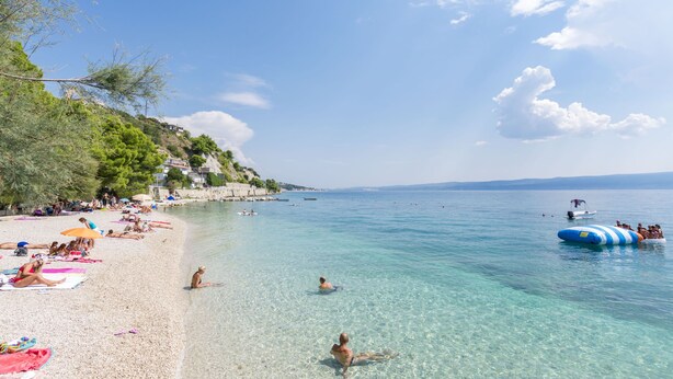A beach with clear water, people sunbathing, and a boat in the distance. - Apartments Cash and Dash (Krilo Jesenice)