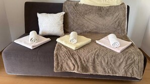 Ein Sofa mit brauner Strukturbezug, ein weißes Kissen und drei zusammengerollte Handtücher in verschiedenen Farben.