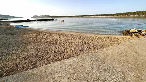 Ein Strand mit Booten, einem felsigen Küstenabschnitt und blauem Himmel.
