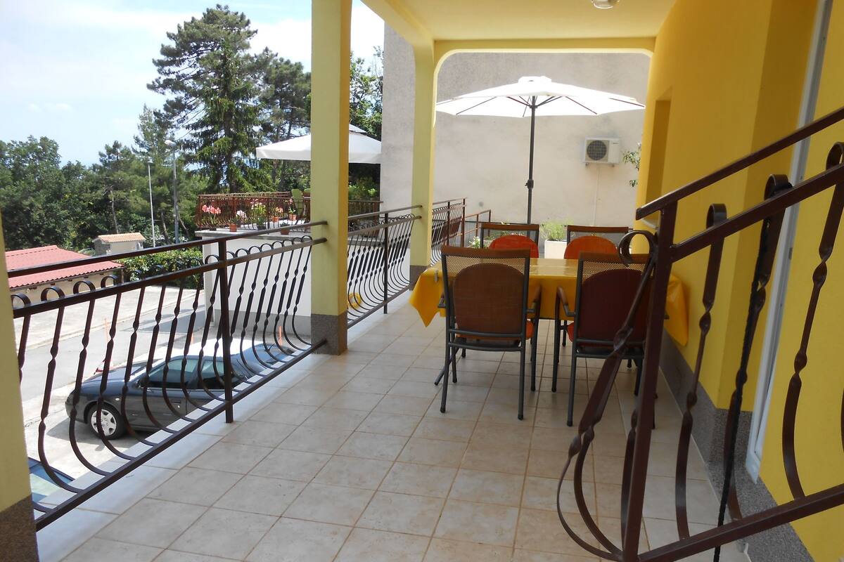 Un balcon avec un sol carrelé, une table avec des chaises et une rambarde.