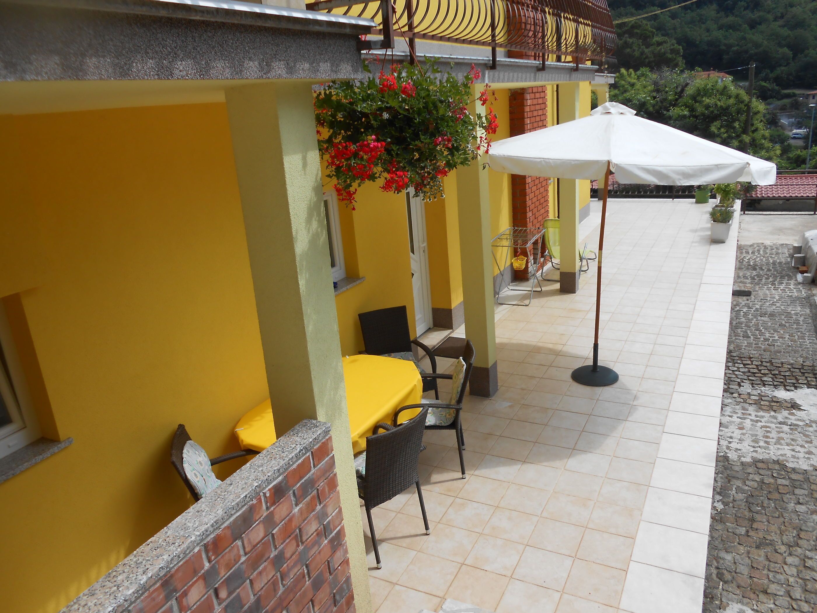 An outdoor seating area with yellow walls, a brick column, and a white umbrella.
