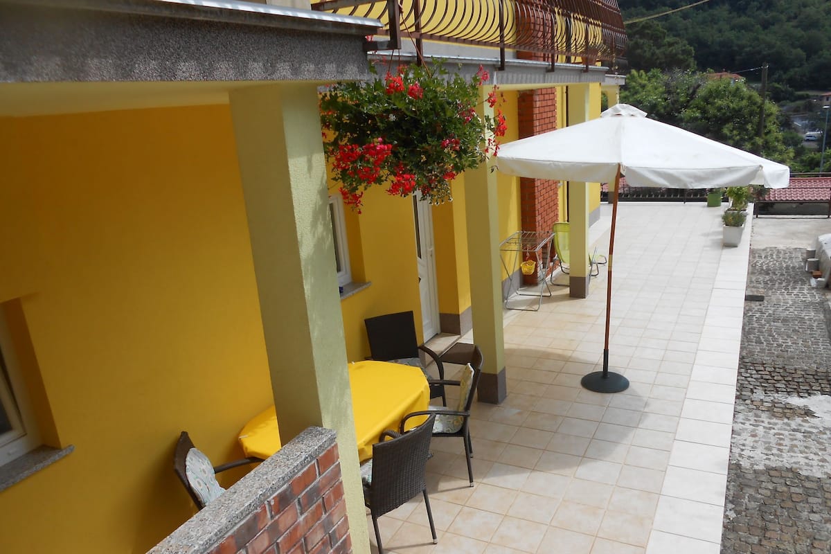 An outdoor patio area with yellow walls, a brick column, a table with a yellow tablecloth, and a white umbrella.