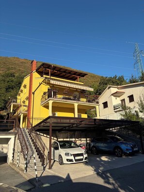 A multi-story yellow building with a covered parking area and a white car parked in front. - Apartments Vesna (Moscenicka Draga)