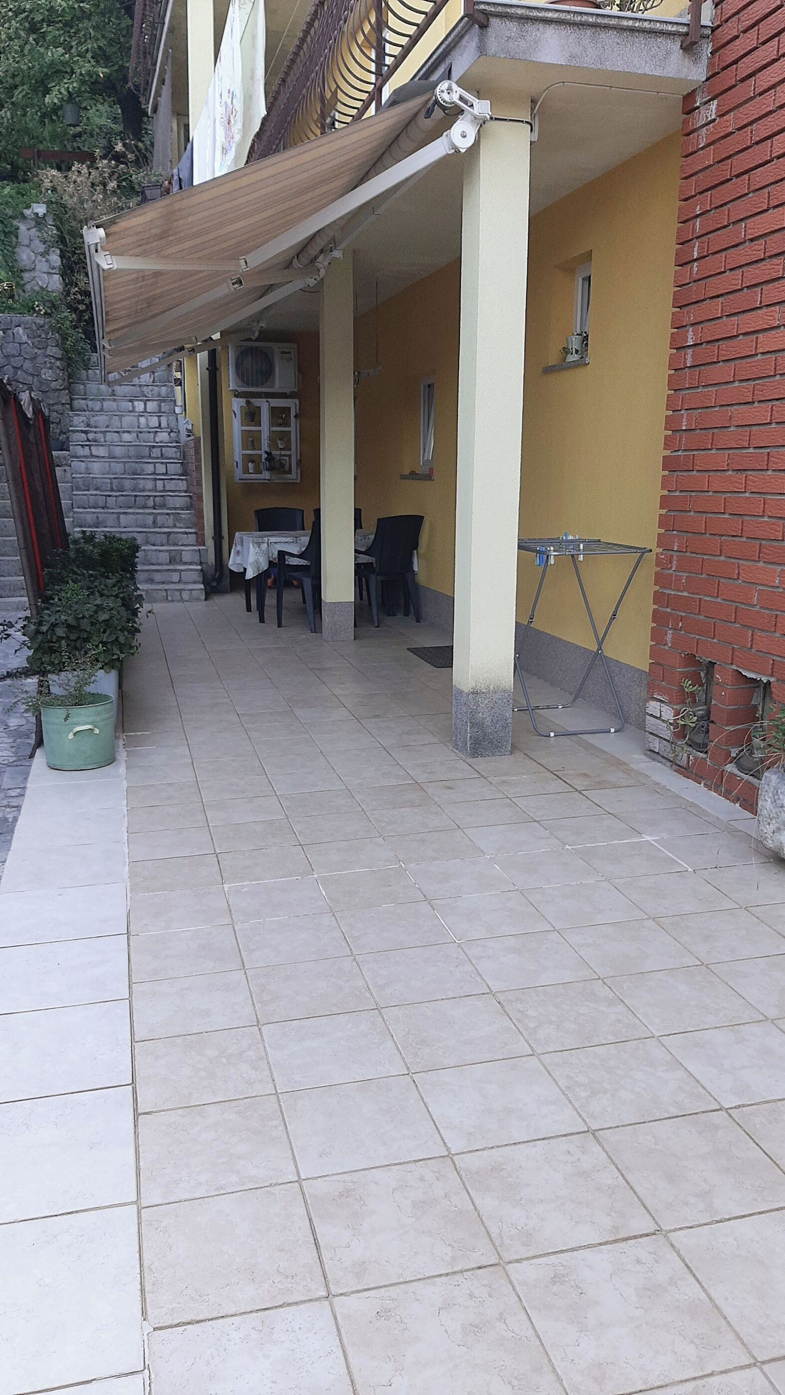 Un espacio al aire libre cubierto con suelo de baldosas, una mesa, sillas y una planta en maceta.