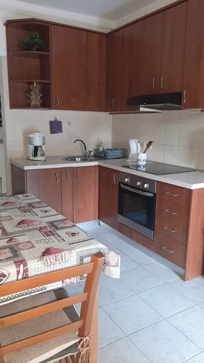 A kitchen with wooden cabinets, a built-in oven, and a dining table with a patterned tablecloth. - Apartments Vesna (Moscenicka Draga)