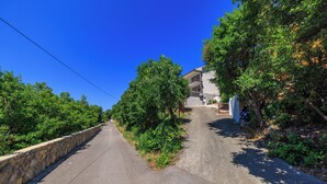 A narrow road flanked by greenery and a stone wall, leading to a building with a balcony. - Apartment Aneta (Povile)