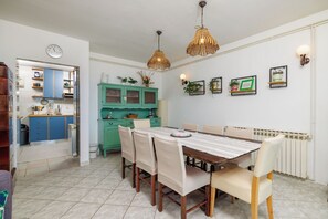 Un comedor con mesa de madera, sillas y una cocina al fondo.