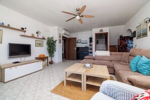 Una sala de estar con televisor, sofá, mesa de centro y ventilador de techo.