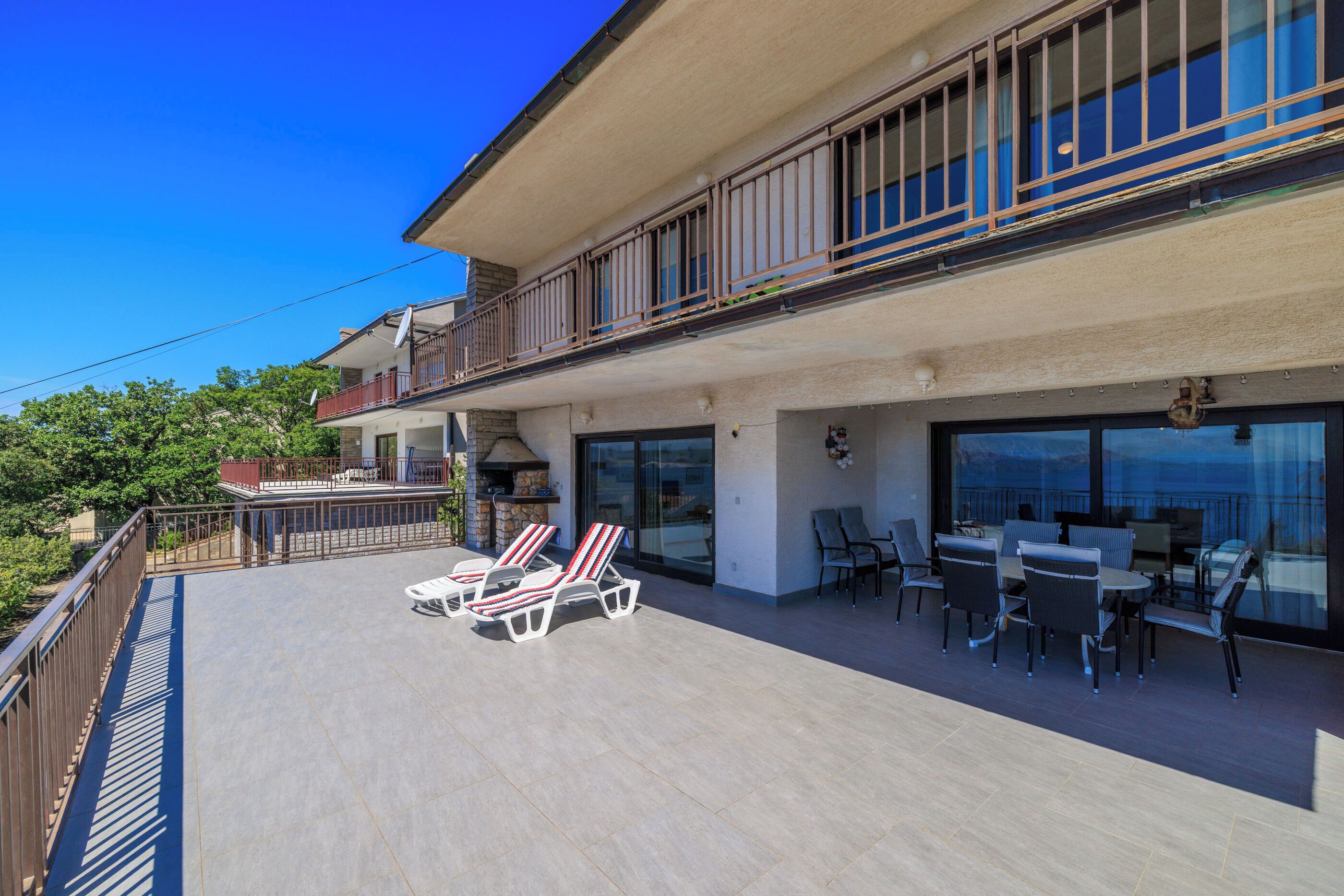 A balcony with sun loungers and a table with chairs, overlooking a scenic view.