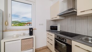 A compact kitchen with a window, a microwave, a stove, and a dishwasher. - Apartments Jozic (Crikvenica)