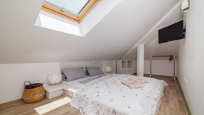 A bedroom with a skylight, a bed with a floral bedspread, a bedside table, and a wall-mounted TV. - Apartments Jozic (Crikvenica)