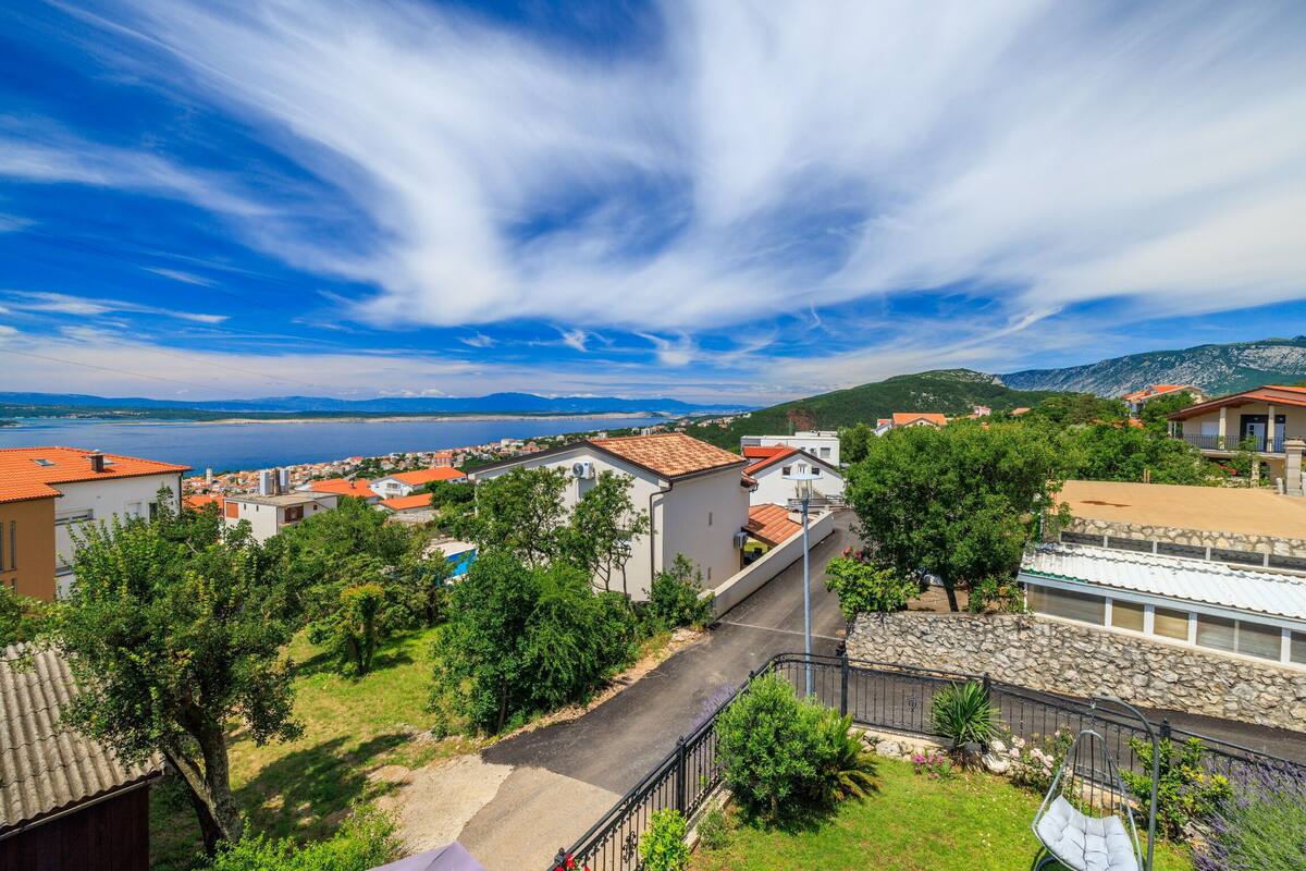 A coastal town with a paved road, stone walls, and buildings with red-tiled roofs.
