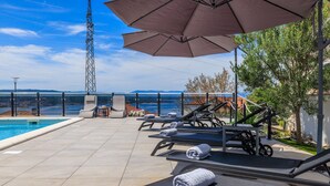 A poolside area with lounge chairs, umbrellas, and a view of the sea. - Apartments Jozic (Crikvenica)