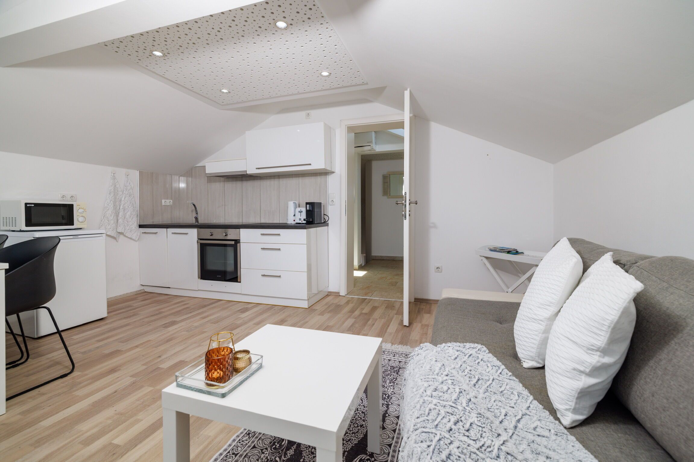 Een modern appartement met een kitchenette, een eethoek en een woonkamer met een bank en kussens.