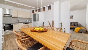 A modern kitchen with white cabinets, a wooden dining table with chairs, and a fruit bowl. - Apartments Jozic (Crikvenica)