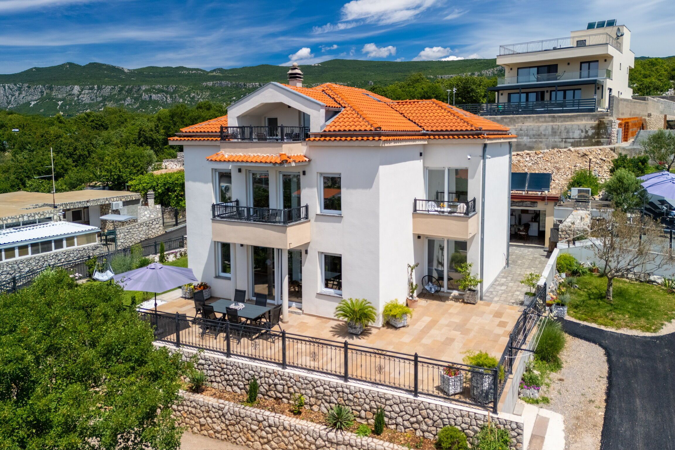 Uma casa de dois andares com varanda, um pátio com móveis de exterior e um muro de suporte de pedra.