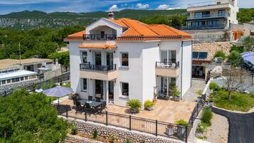 Uma casa de dois andares com varanda, um pátio com móveis de exterior e um muro de suporte de pedra.