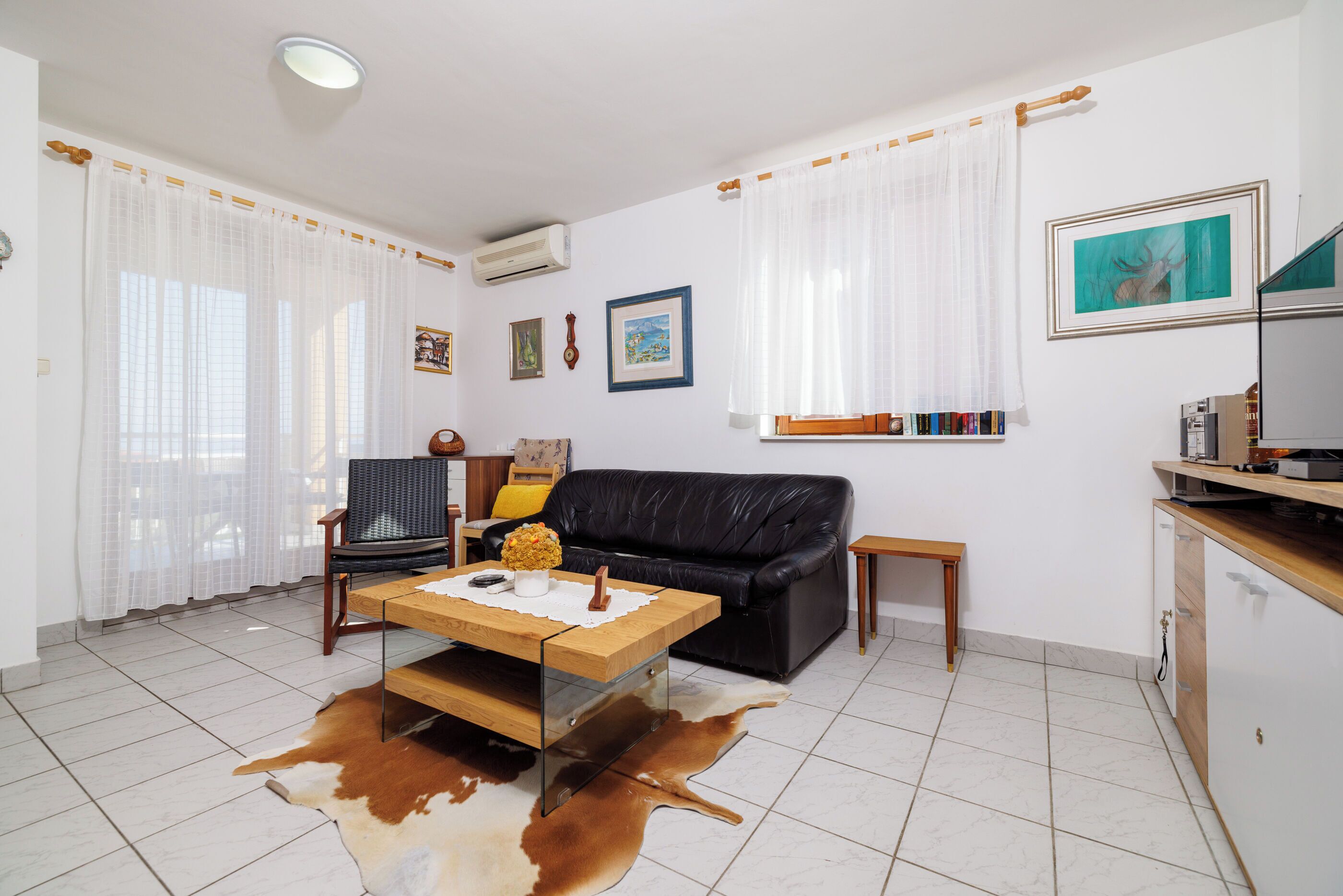 Ein Wohnzimmer mit Ledersofa, Couchtisch aus Holz, Kuhfellteppich und Bücherregal.