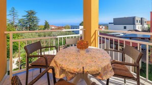 Ein Balkon mit Korbstühlen, einem Tisch mit blumigem Tischläufer und einer Blumenvase.
