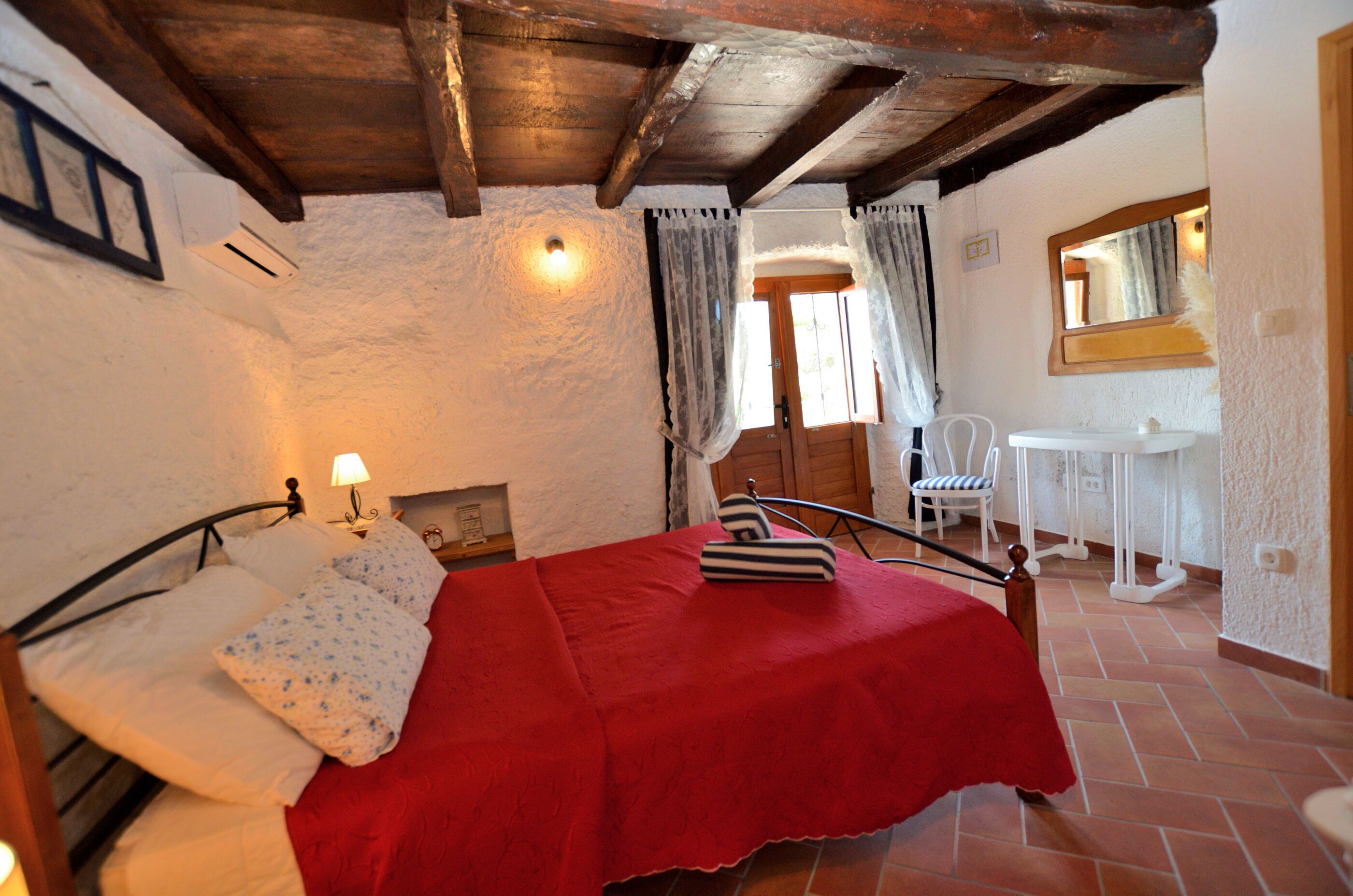 A bedroom with a bed, a nightstand, a chair, a small table, and a window with curtains.