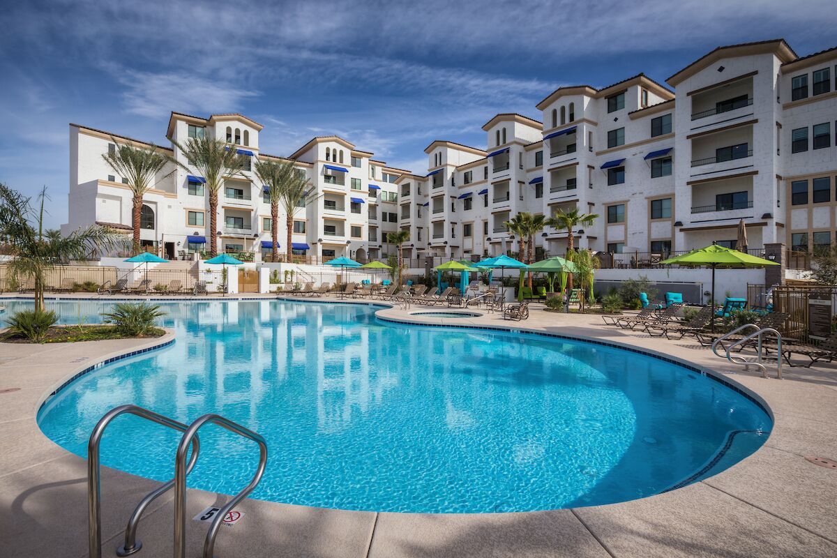 A swimming pool with lounge chairs and umbrellas, surrounded by multi-story buildings with balconies.