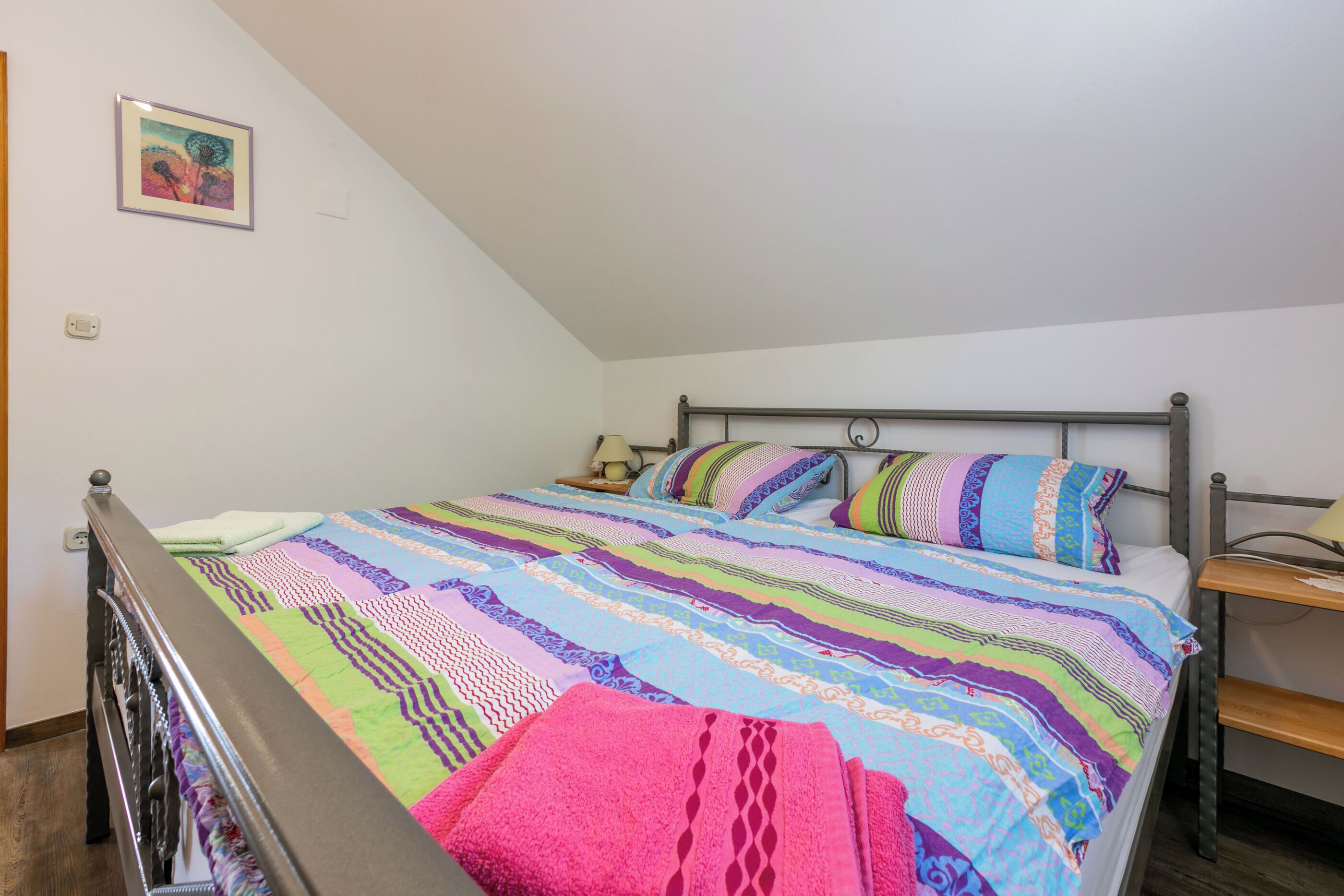 A bedroom with a bed, a nightstand, a lamp, and a picture on the wall.
