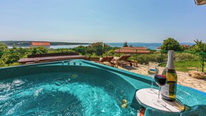 Una piscina con vista sul mare, una bottiglia di vino e sedie a sdraio.