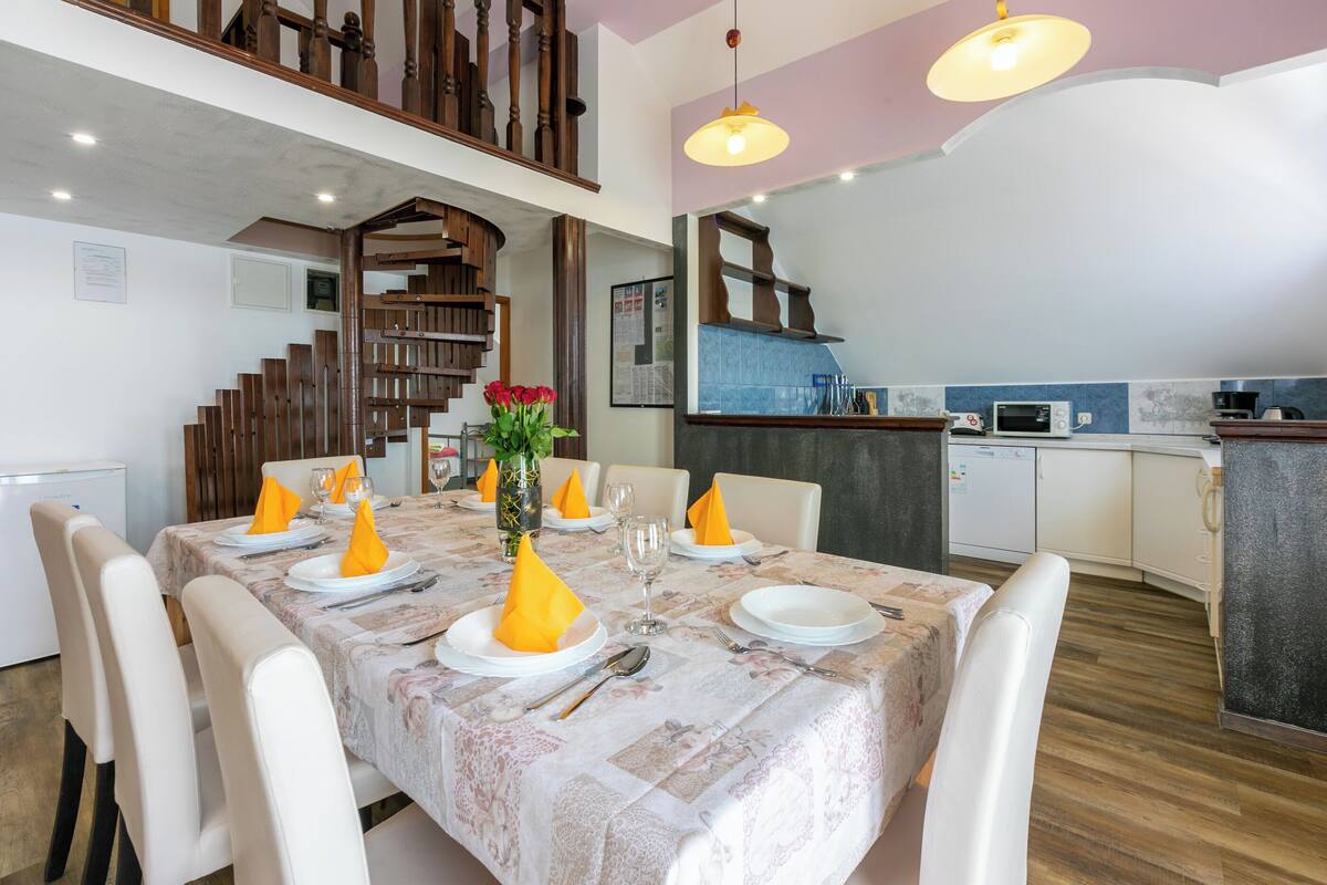 A dining area with a table set for six, a staircase, and a kitchen area.