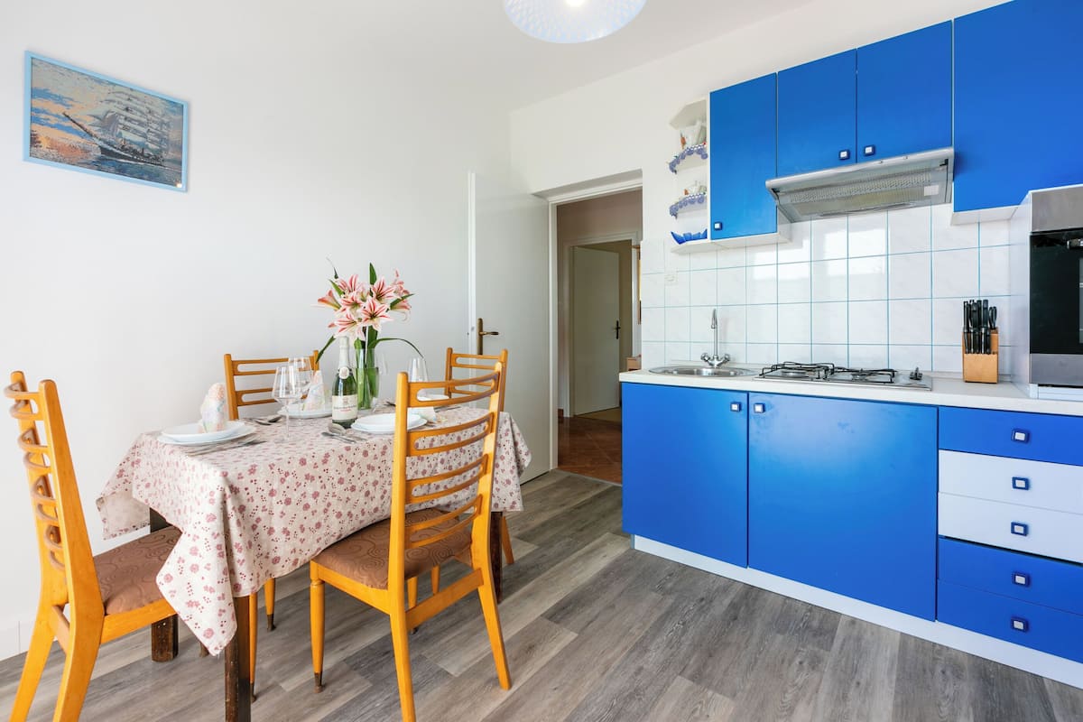 A modern kitchen with blue cabinets, a white countertop, and a dining area with a floral tablecloth.