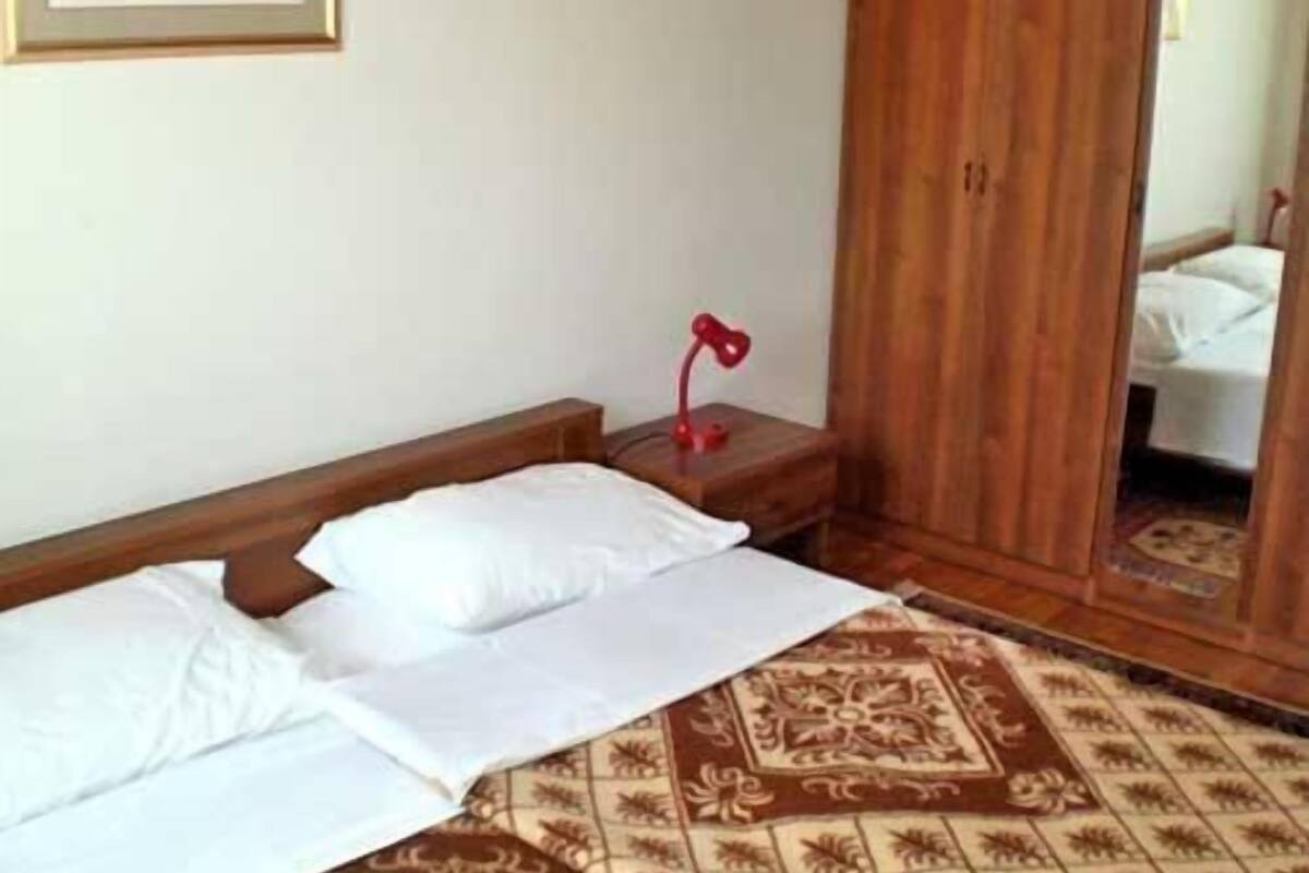 A hotel room with a bed, a nightstand, a red lamp, a wooden wardrobe, and a red-framed mirror.