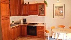 A compact kitchen with wooden cabinets, a dishwasher, and a dining area with a table and chairs. - Apartment Anto (Umag)