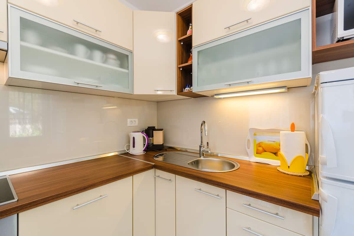 A modern kitchen with white cabinets, a stainless steel sink, and a wooden countertop.