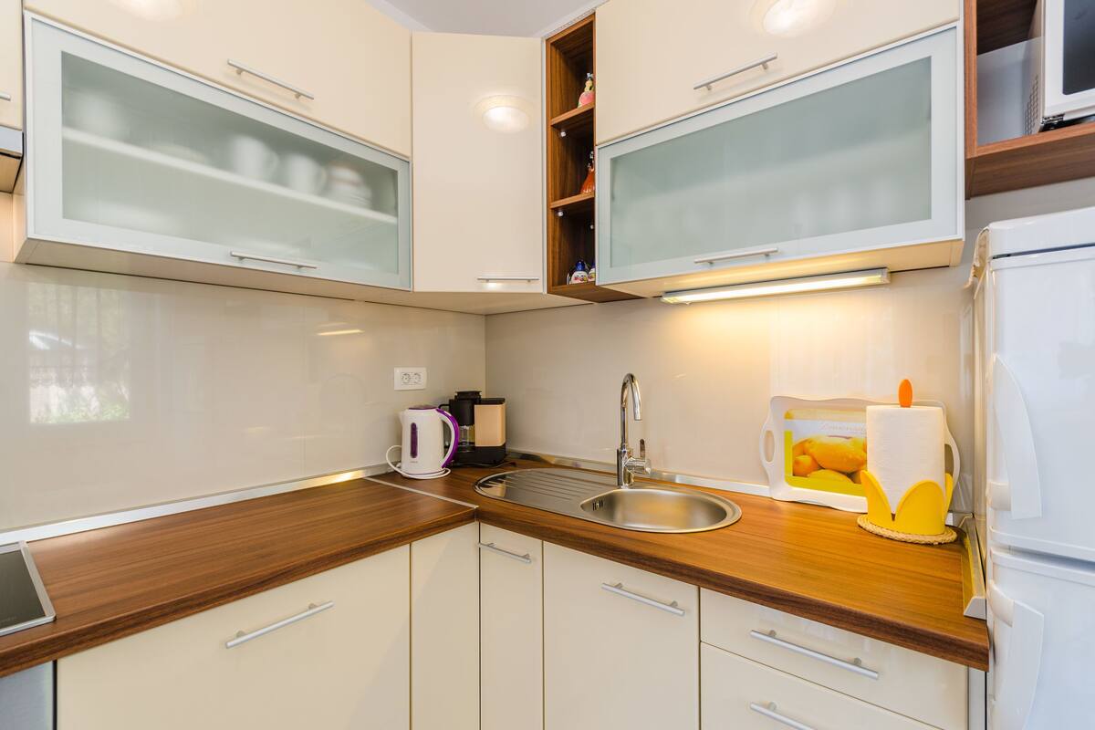 A modern kitchen with white cabinets, a stainless steel sink, and a wooden countertop.