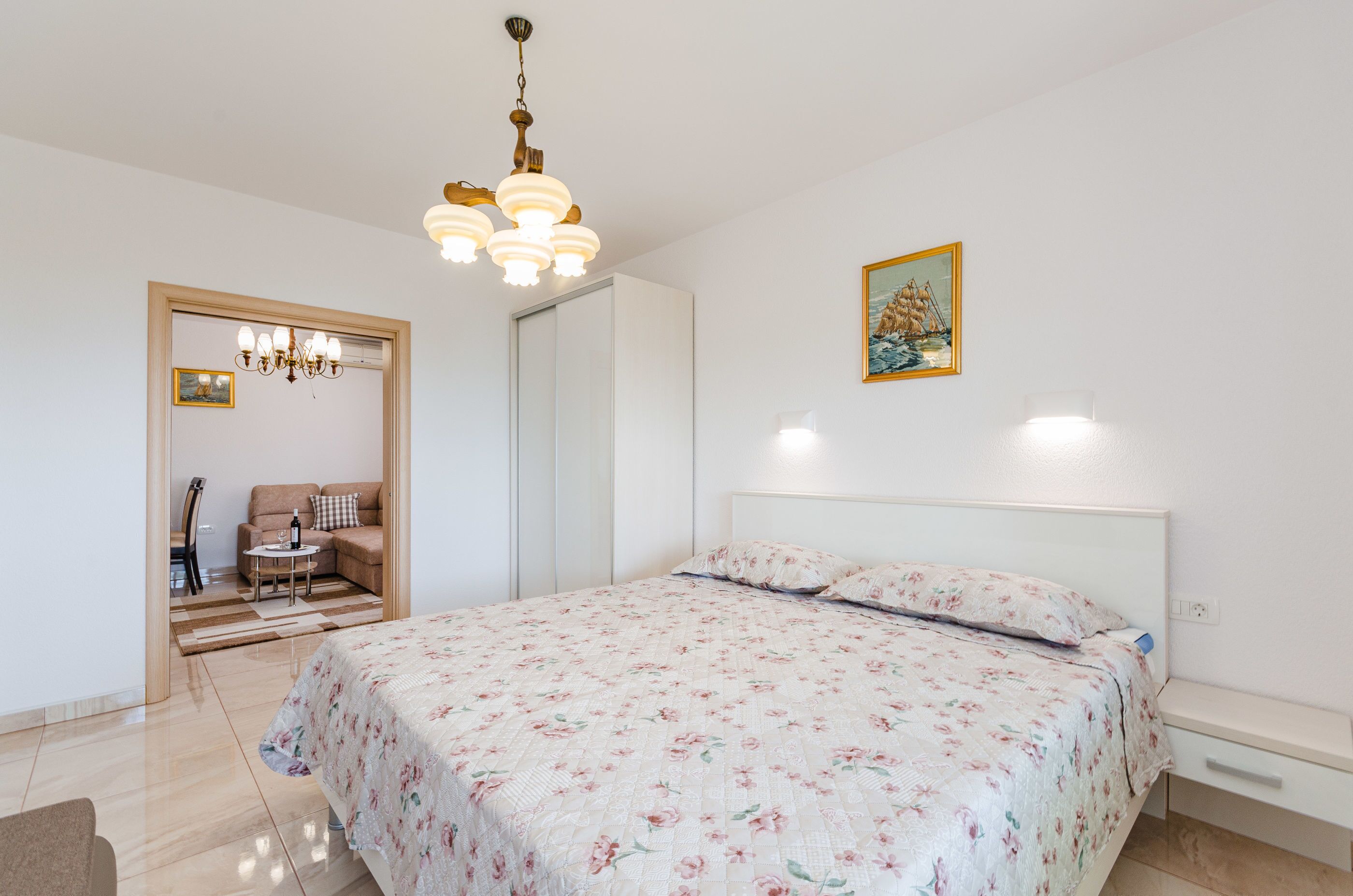 Un dormitorio con cama, mesita de noche, sillón, sofá, candelabro y un cuadro en la pared.