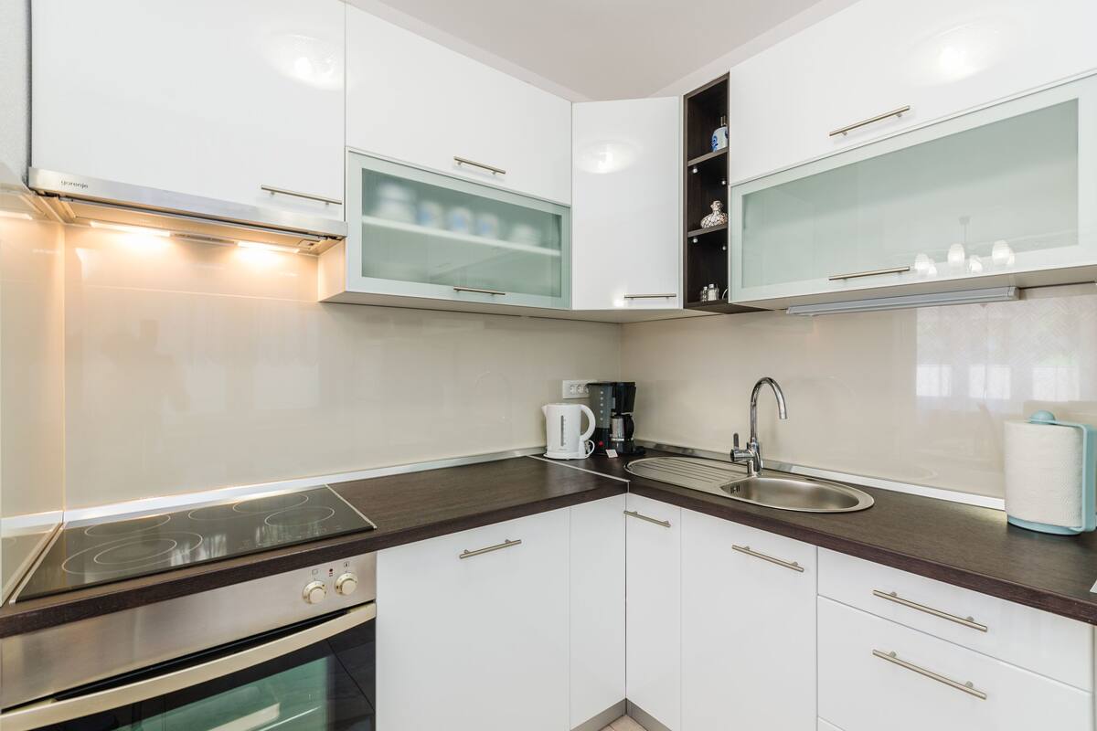 A modern kitchen with white cabinets, a stainless steel stove, a sink, and a coffee maker.